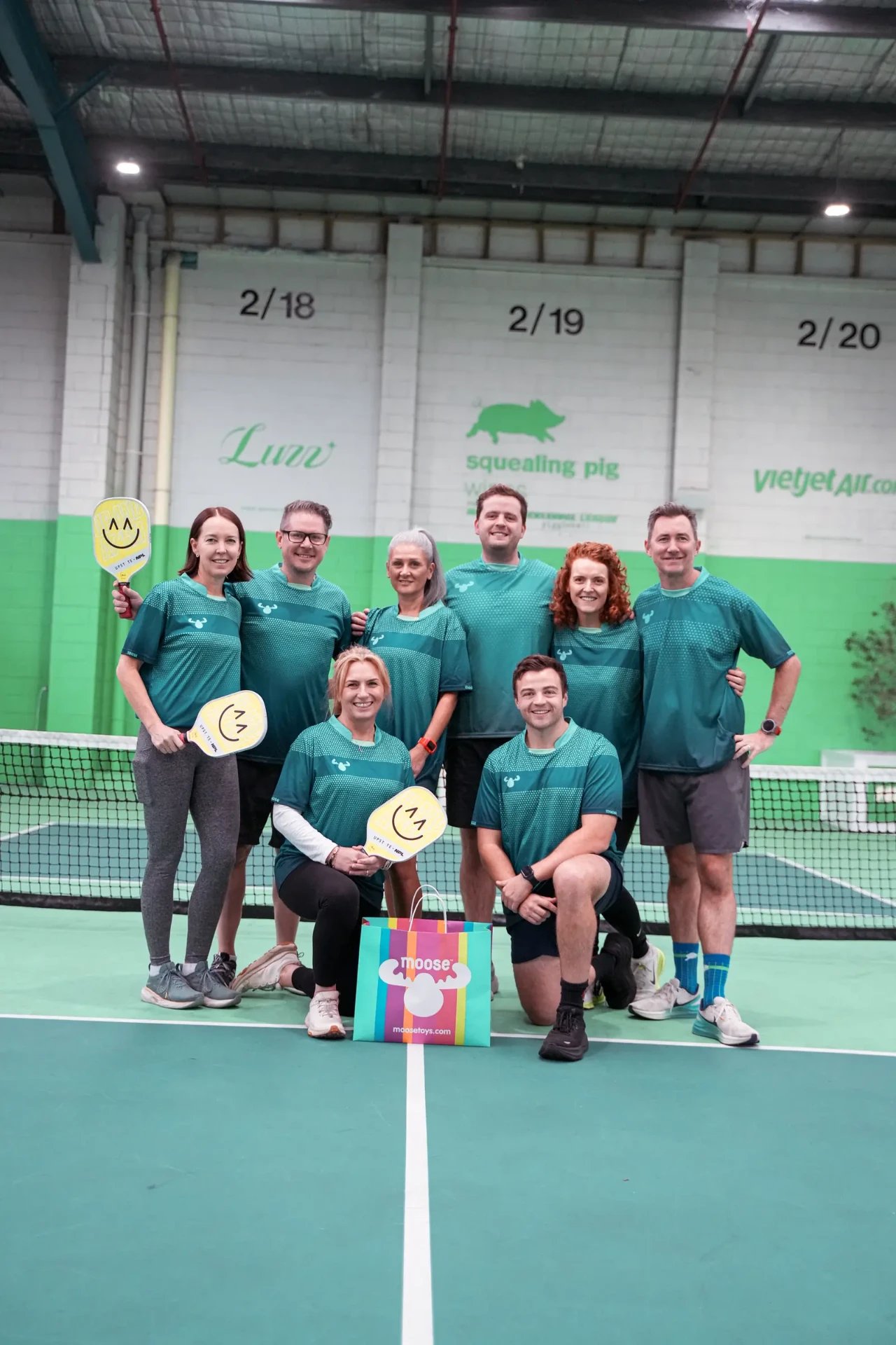 A corporate pickleball team posing together on court at The Jar South Melbourne