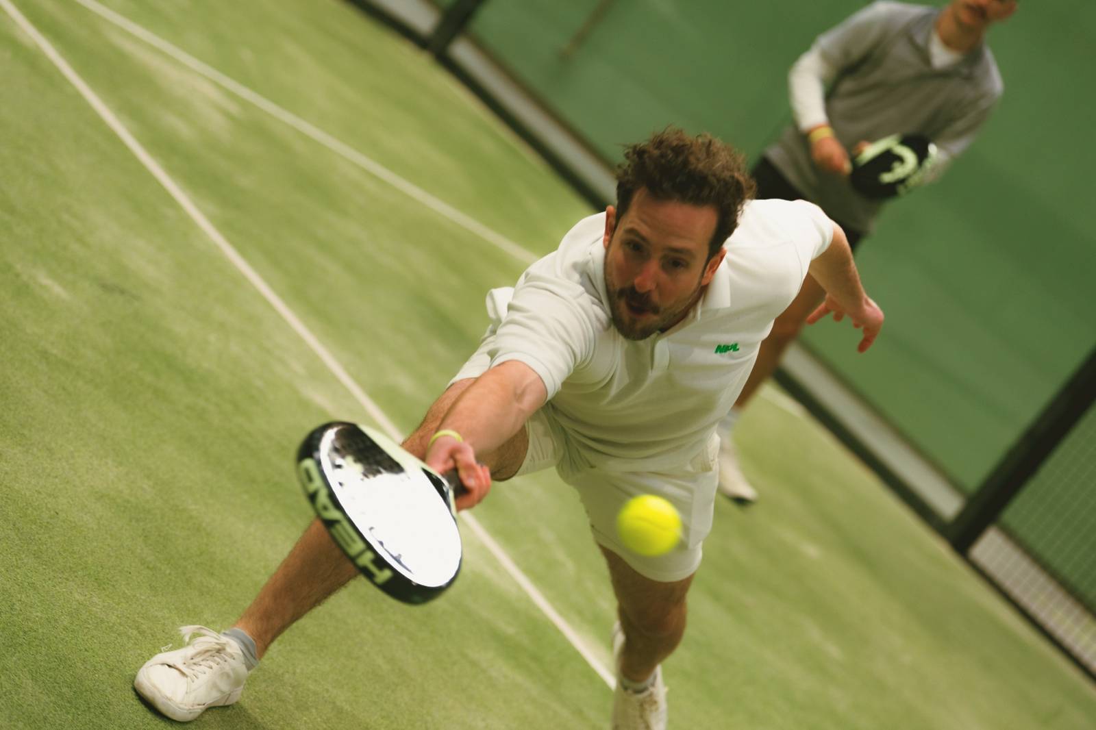 A padel player stretching for a low ball at Maidstone